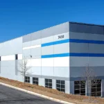 Contemporary industrial building exterior featuring white and grey paneling, blue accent stripes, large windows, building number 7450, and modern landscaping in Atlanta commercial development