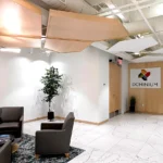 Modern office reception area featuring geometric ceiling panels, grey lounge chairs, live plant, marble flooring, and branded wall signage in Atlanta corporate space