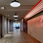 Modern office hallway with illuminated Caliburn branding, wood slat wall details, and pendant lighting demonstrating CCG's attention to architectural details