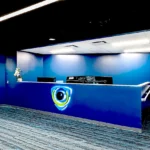 Sleek reception desk featuring illuminated EyeQ logo, navy blue walls, modern lighting, and patterned carpet designed by Cornerstone Contracting