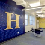 Custom educational branding wall designed by Cornerstone, commercial construction company Atlanta, featuring illuminated university logo and mission statement