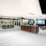 Luxurious reception area at Lucid Buckhead featuring custom wood-slat desk, stone accent wall with circular mirrors, and floor-to-ceiling windows by Cornerstone Contracting
