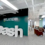 Signature brand wall at Relatient featuring dimensional 'Dash' lettering, teal accent wall, leather lounge seating, and exposed ceiling by Cornerstone Contracting