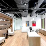 Welcoming lobby space at Sisecam Atlanta featuring custom display shelving, white seating area, exposed ceiling design, and brand-integrated wall elements by Cornerstone Contracting