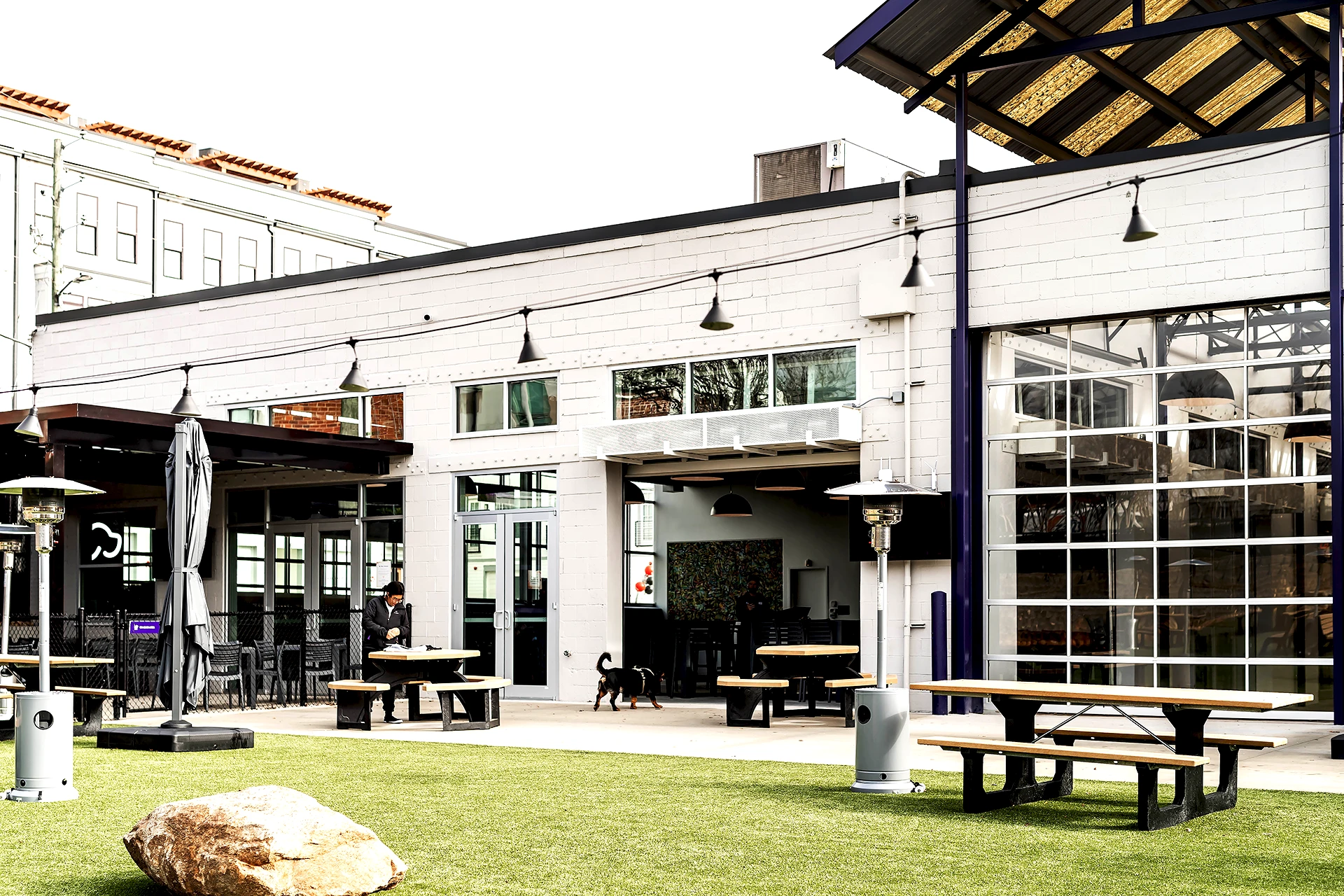 Indoor-outdoor social space featuring large roll-up doors connecting interior and exterior areas at Skiptown pet facility built by BuiltByCCG